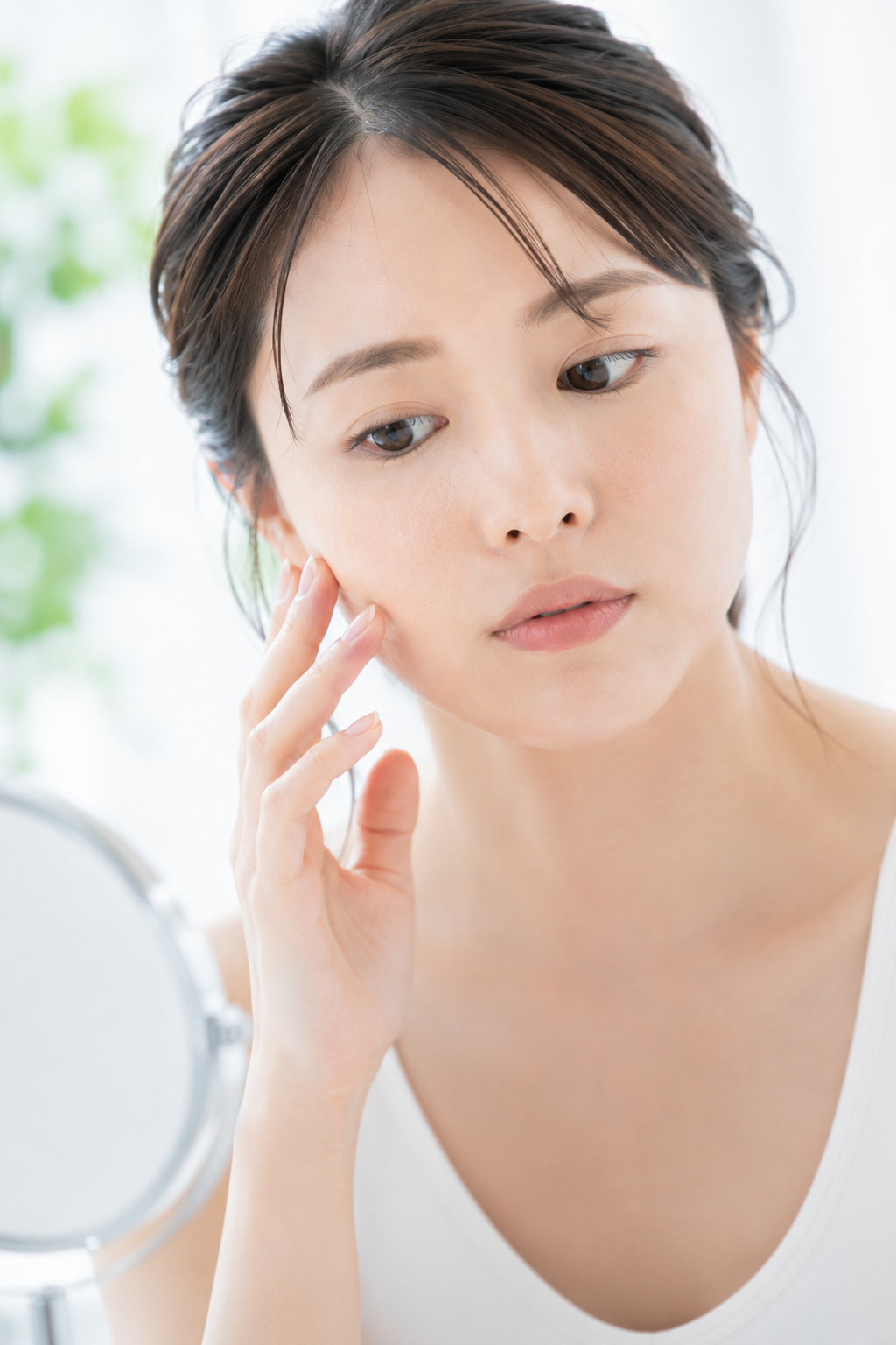 鏡を見ながら頬の毛穴を気にする女性